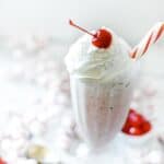 A single sundae glass filled with peppermint shake, whipped cream, and a cherry.