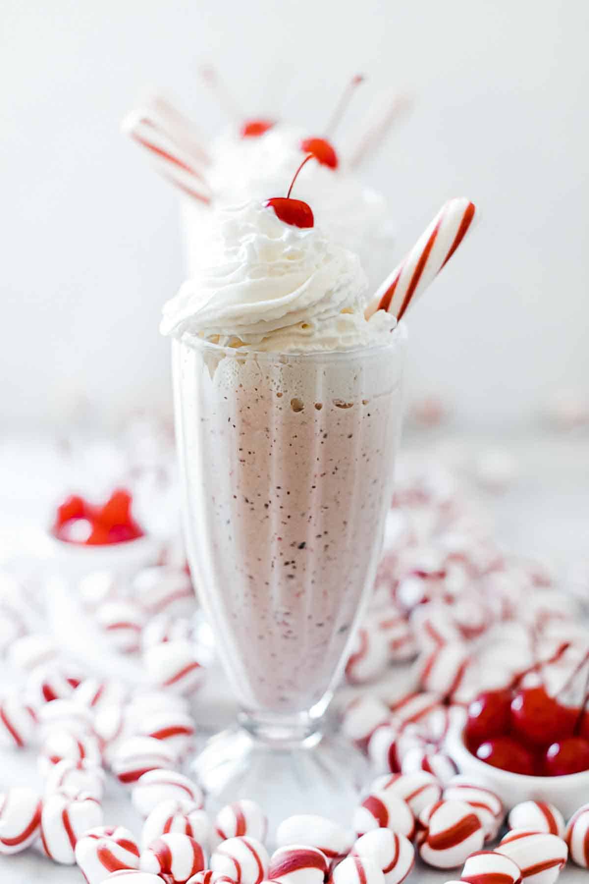 Peppermint shake in sundae glasses. They are lined up and garnished with whipped cream and a cherry.