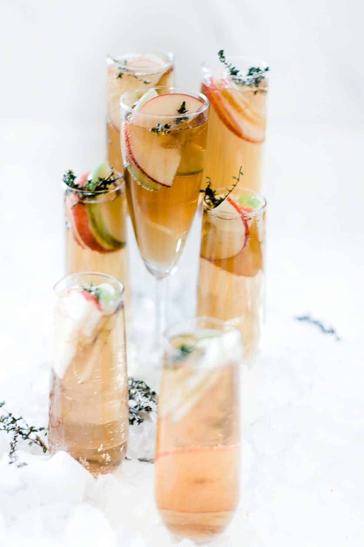 Thanksgiving punch in champagne glasses. They are all various sizes and garnished with apple slices and thyme.