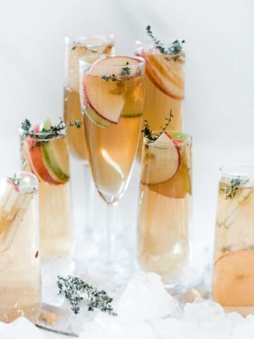 Thanksgiving punch in various sizes of champagne glasses. The are garnished with apple slices and thyme.