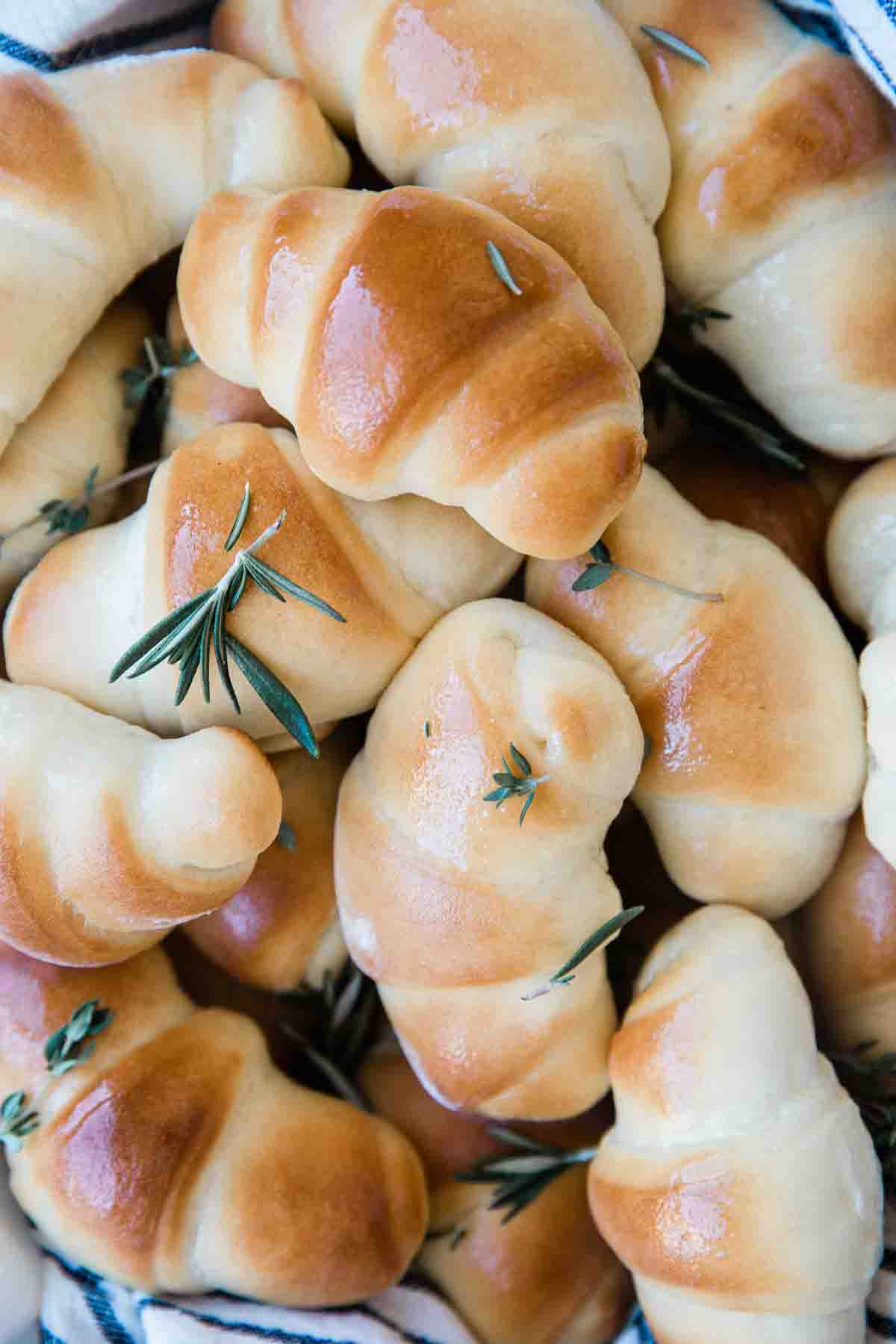 A close up of crescent rolls. They are brushed with butter and sprinkled with rosemary.