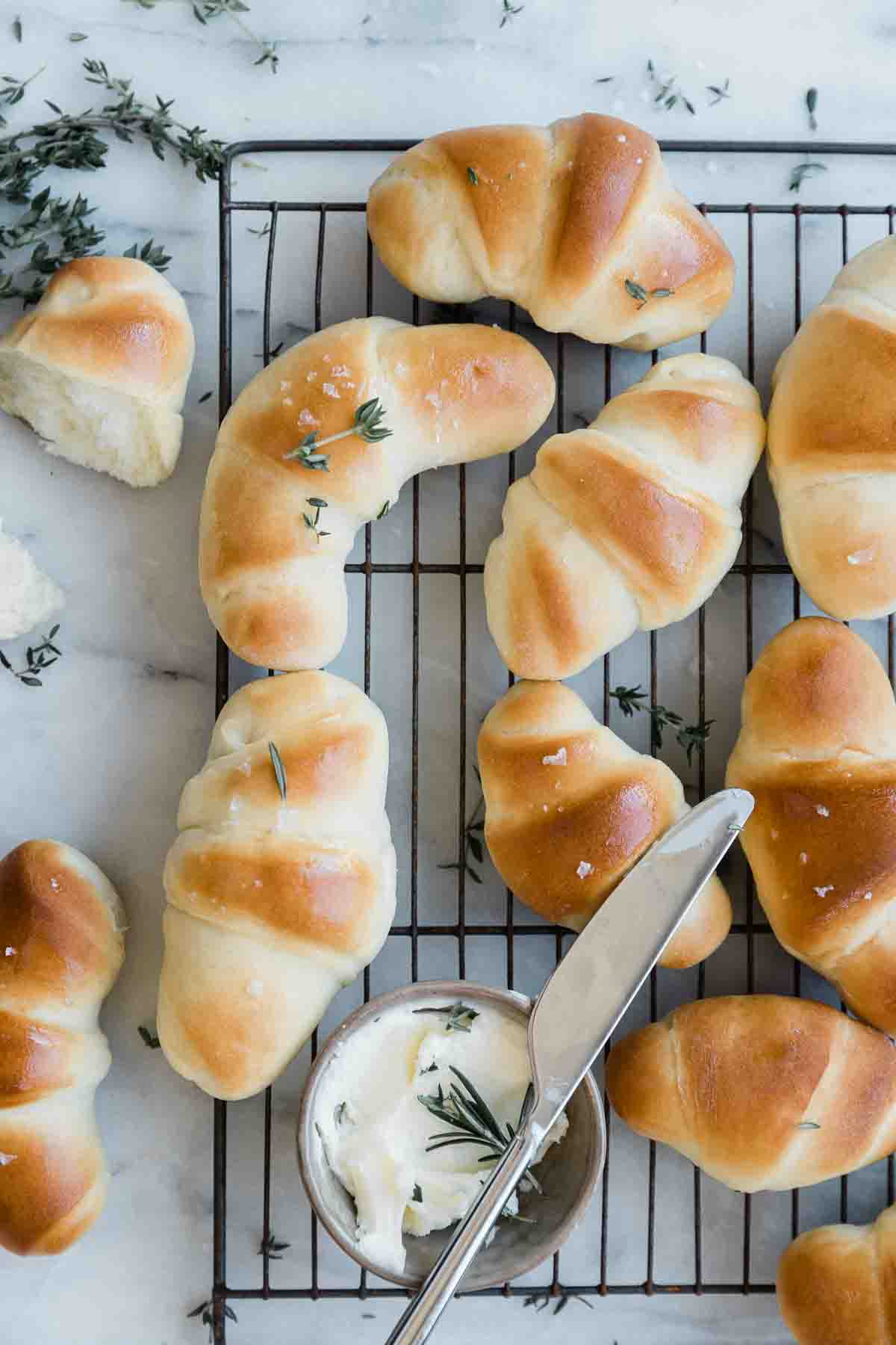 Crescent roll recipe rolls on a cooling rack. There is a small bowl of butter to the side.