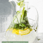 A glass and pitcher full of cucumber, lemons and herbs.