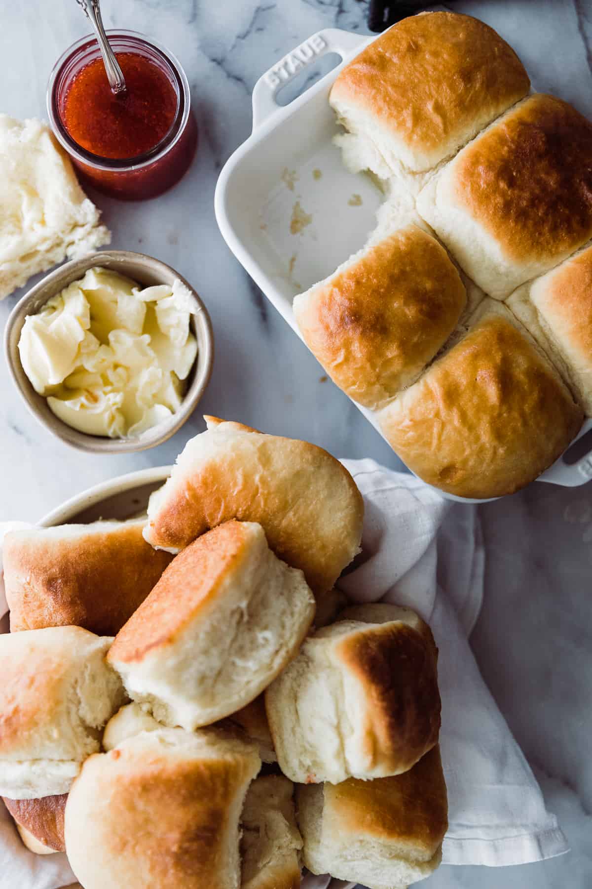 A bowl and pan of golden brown rolls with a small bowl of butter. 