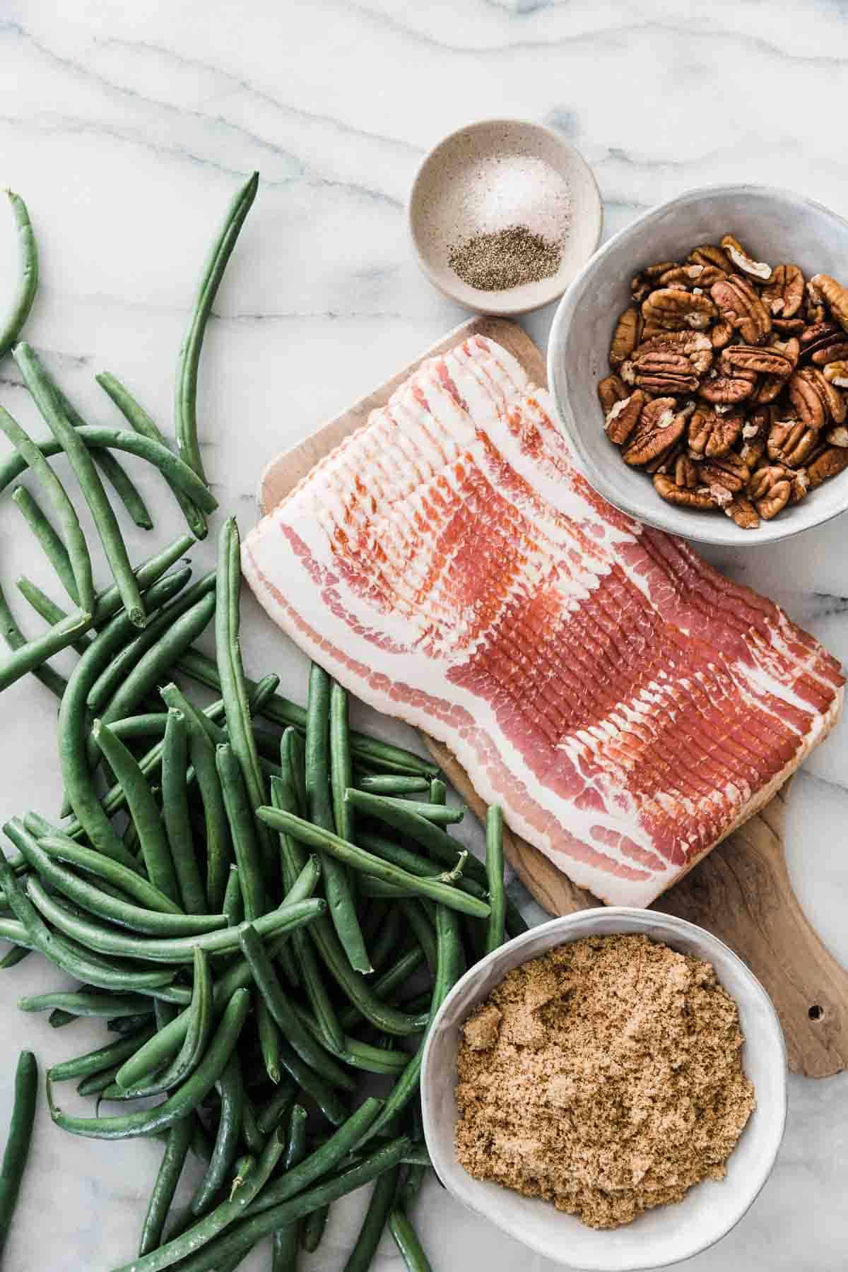 Bacon, green beans, pecans, brown sugar, and salt and pepper on a marble counter.