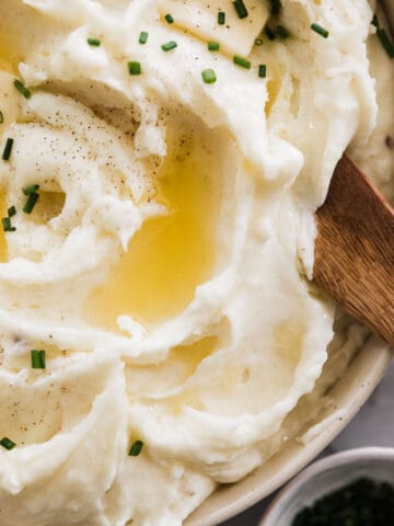 Instant pot mashed potatoes in a white bowl topped with chives and a wooden spoon.