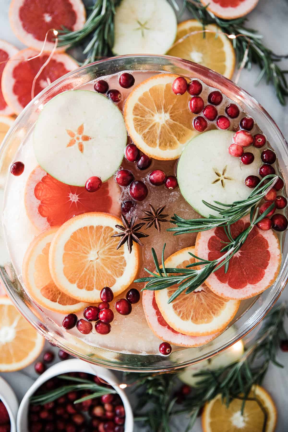 Large glass bowl of slushy bubbly drink with cranberries, sliced oranges and apples as garnishes. 