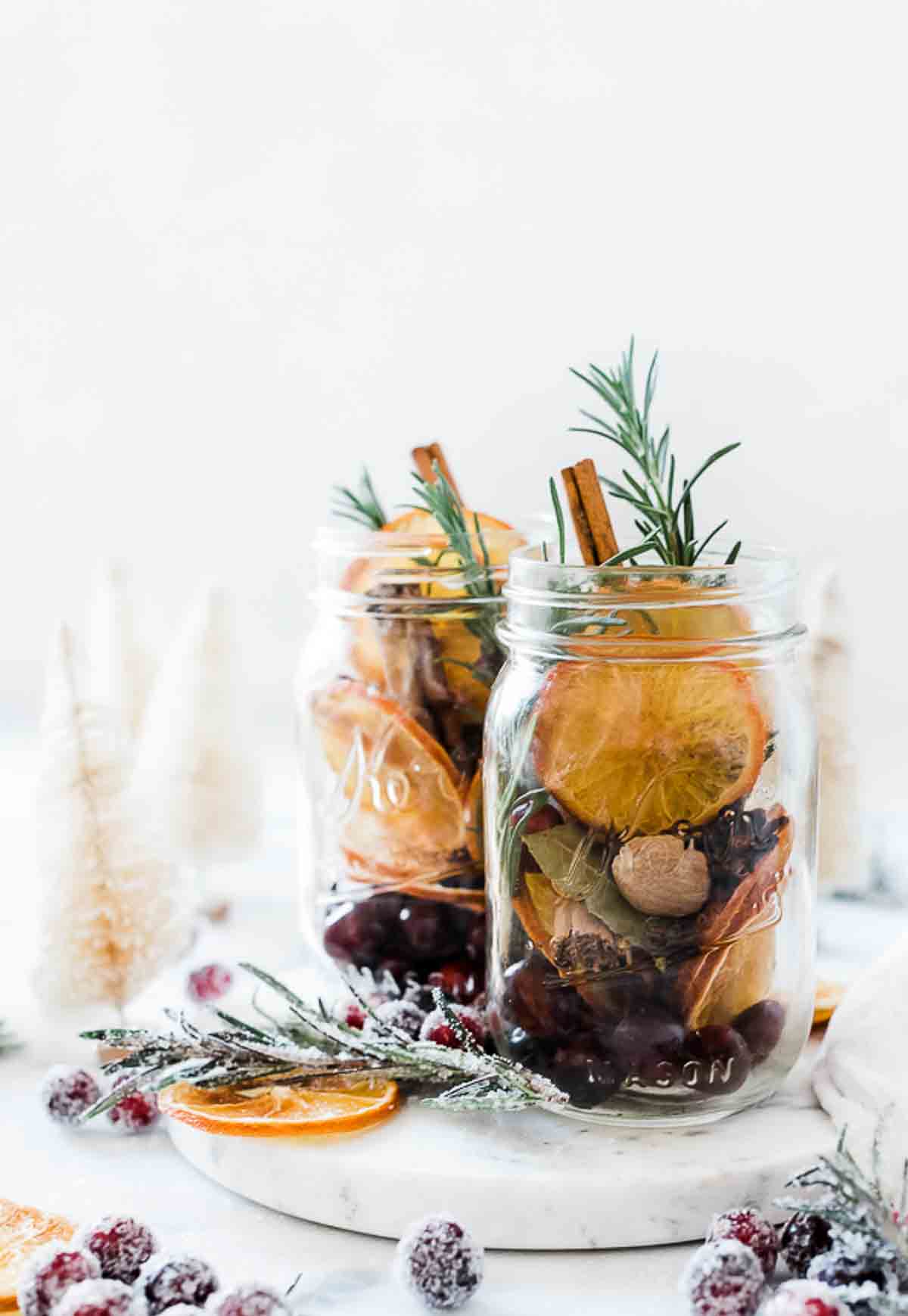 Two mason jars filled with christmas potpourri. There are sugared cranberries to the side.
