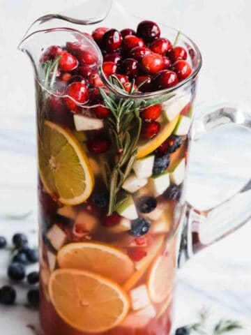 Non alcoholic sangria in a tall glass jar. There are blueberries to the side.
