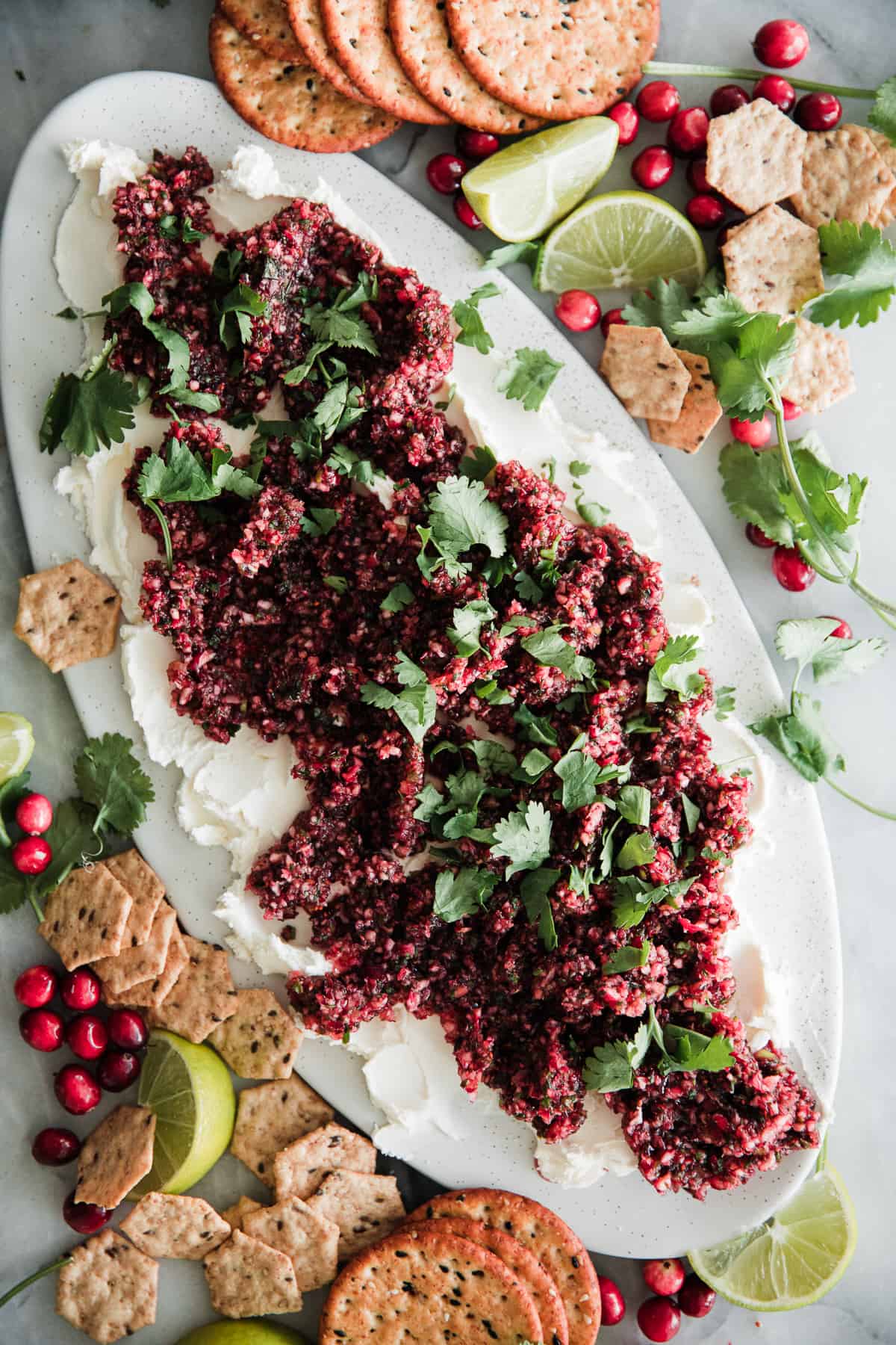 Cranberry salsa on top of cream cheese on an oval platter with cilantro garnish and crackers to the side. 