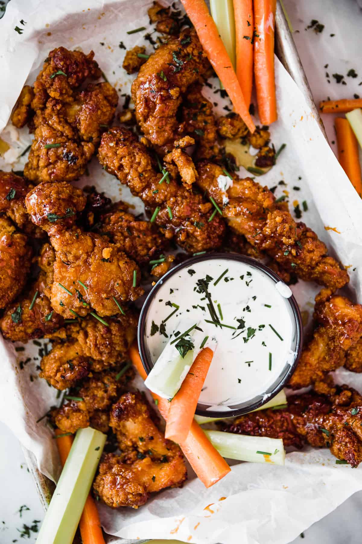 Sticky breaded chicken strips on tray with ranch dipping sauce and carrot and celery sticks. 