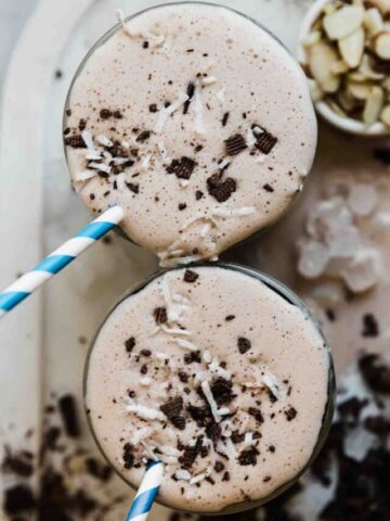 An overhead shot of two glasses filled with chocolate protein smoothie. They are garnished with shaved chocolate.