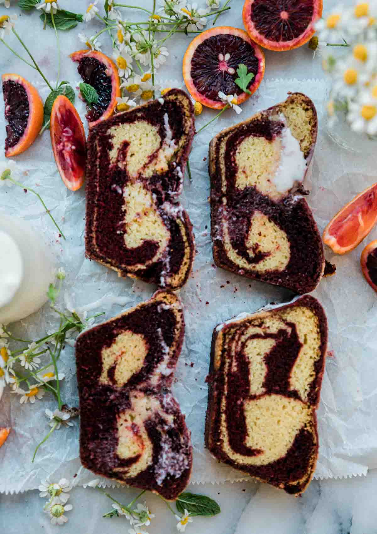 Sliced velvet loaf layed on a marble counter. There is oranges and flowers to the side.