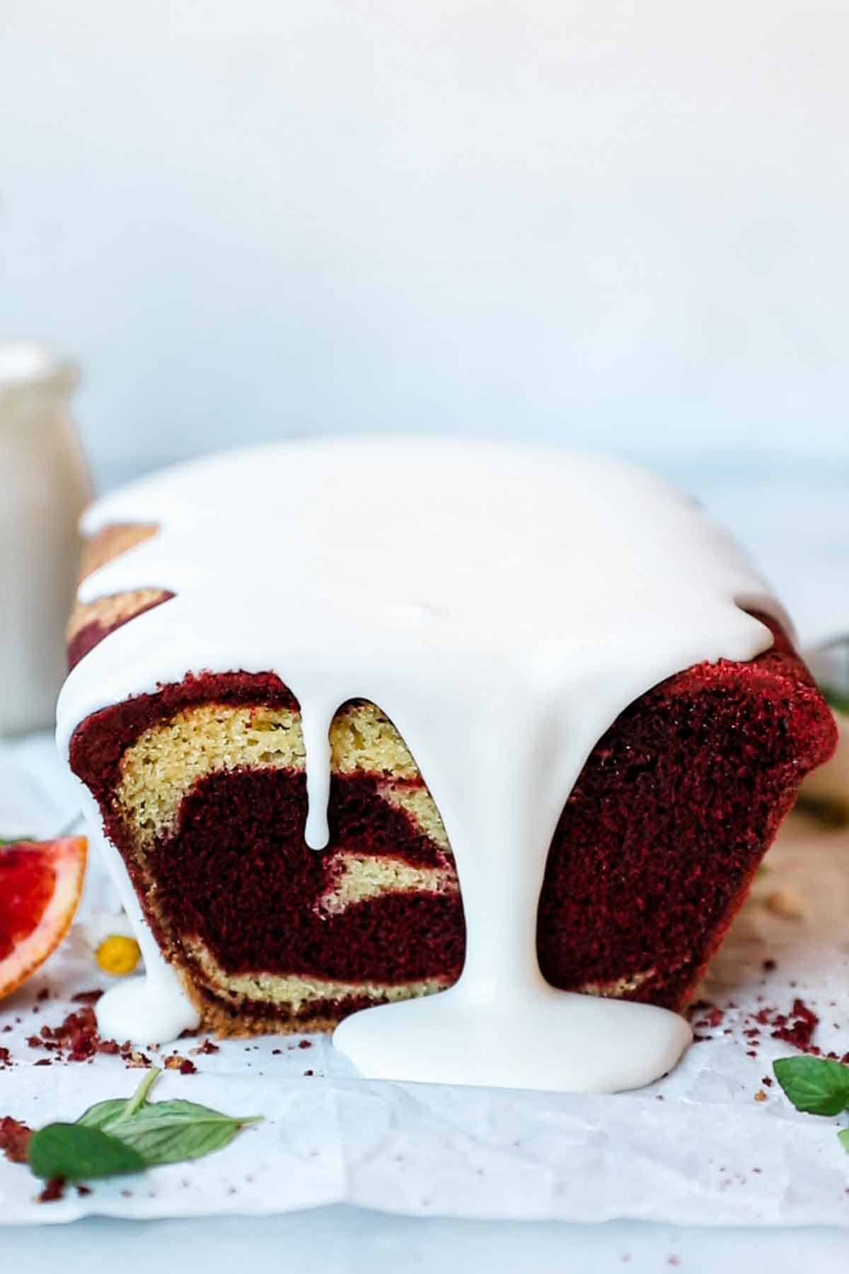 A loaf of red velvet marble bread. There is glaze dripping off the front.