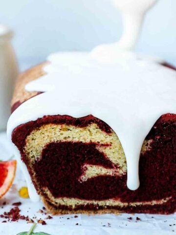 Red velvet Loaf on a white counter. There is glaze being drizzled on top.