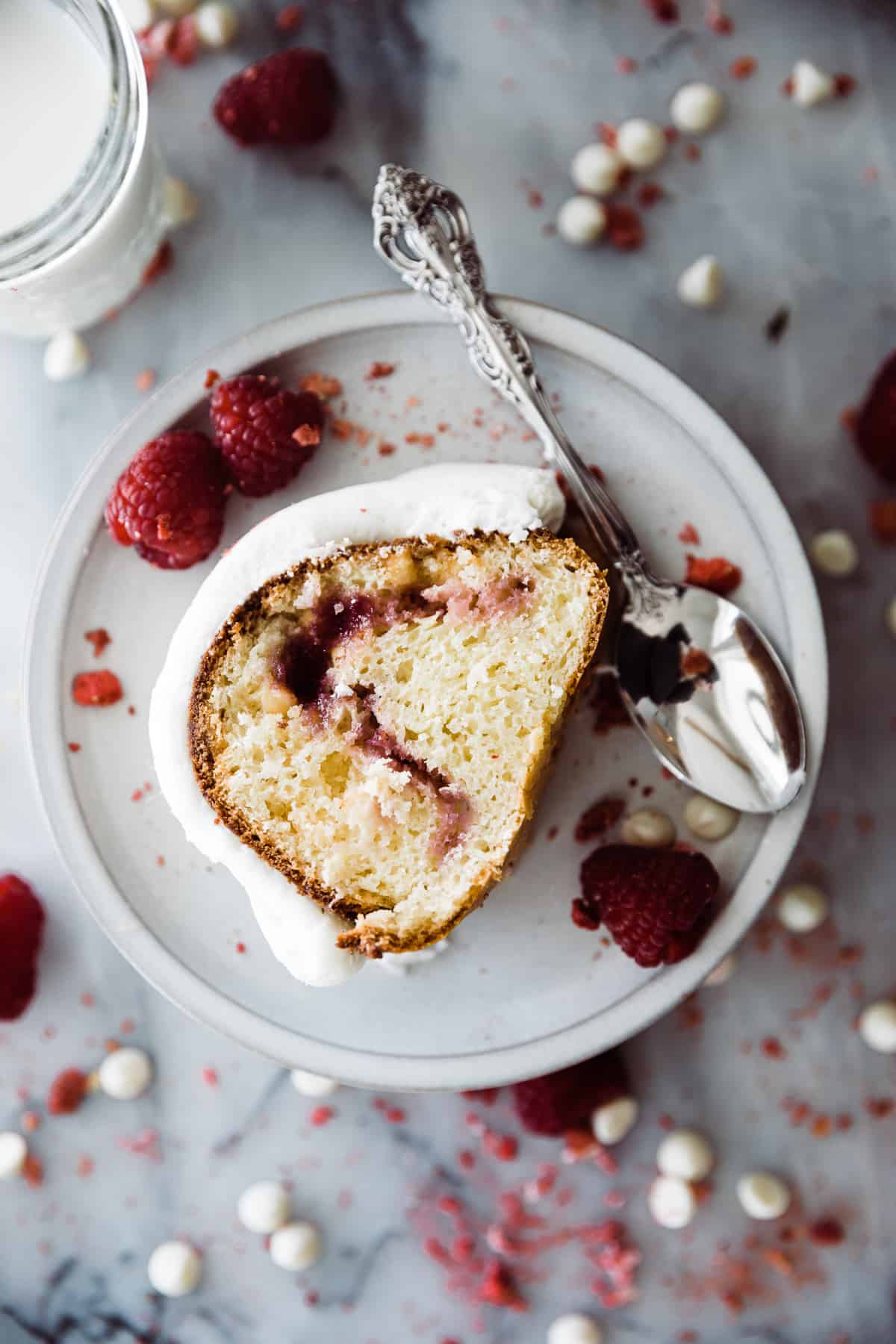 A slice of white cake with cream cheese frosting and red swirled raspberry preserves on plate. 