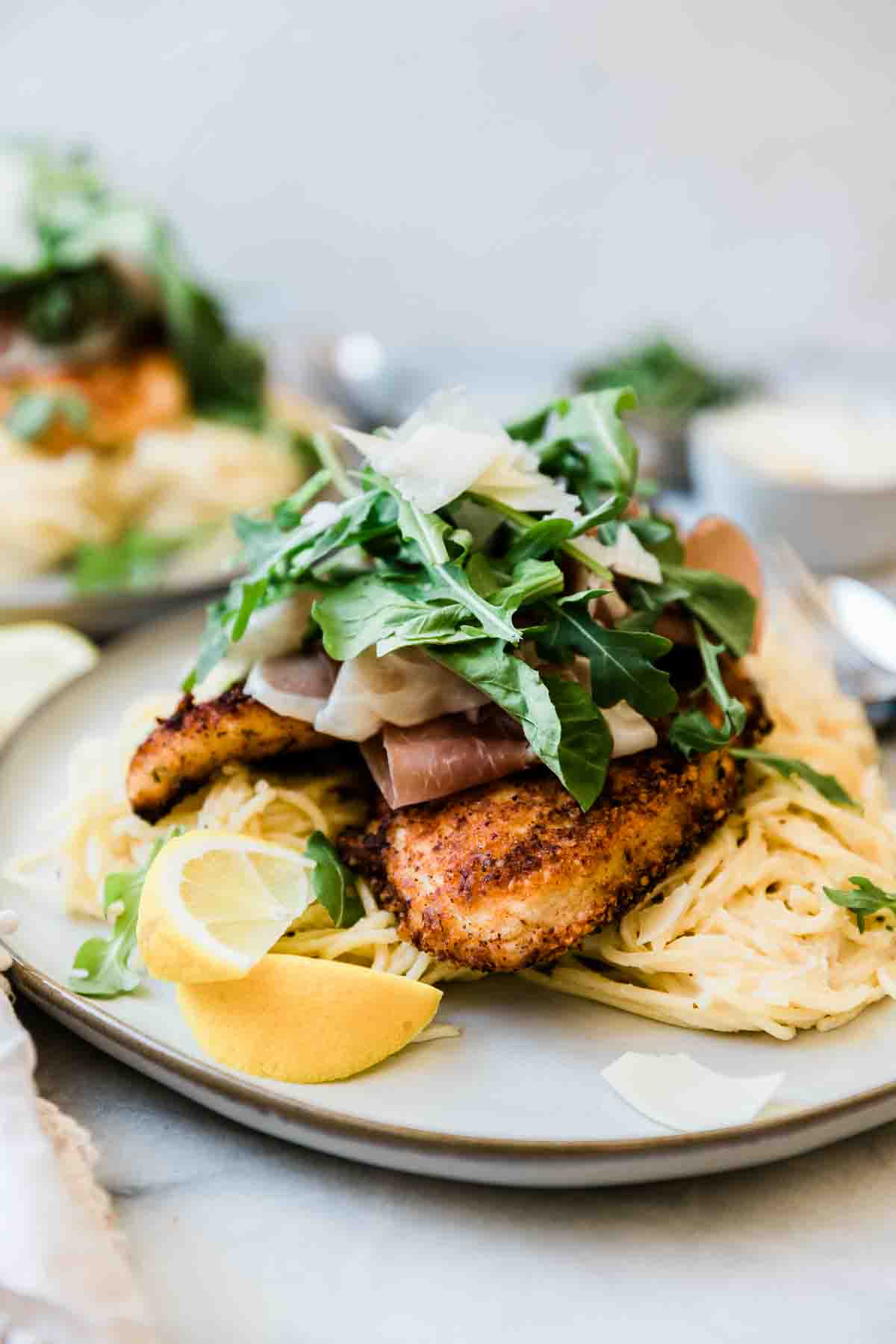 grilled chicken, spaghetti, prociutto, and arugula piled high on a grey plate.