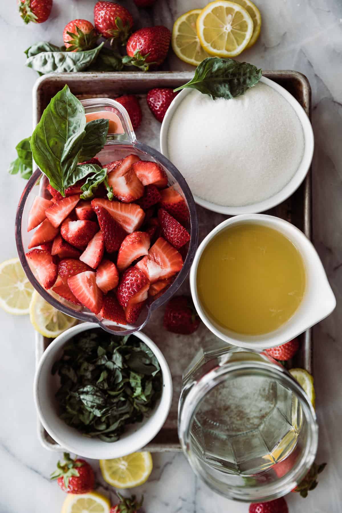 bowls of strawberries, basil, lemon juice, sugar and water on a tray. 
