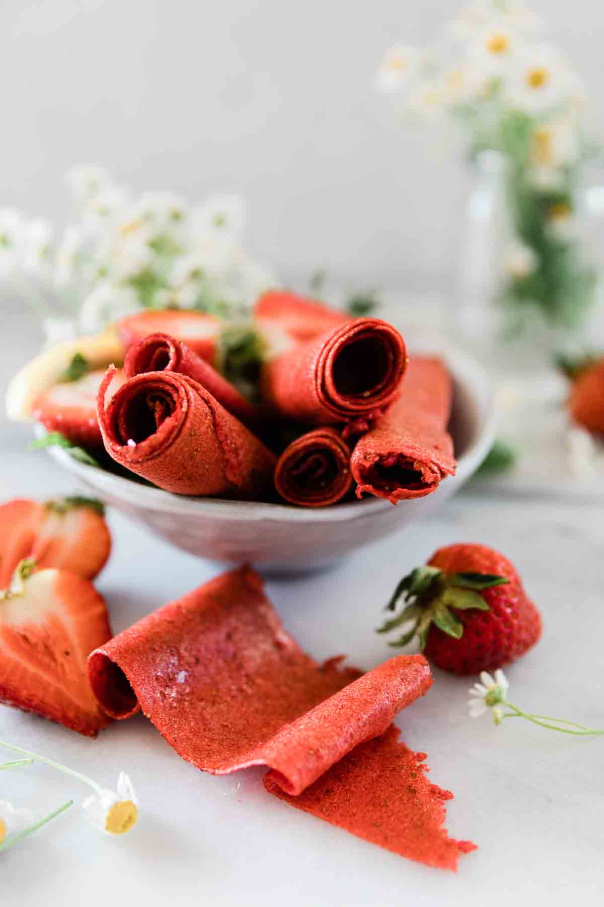Homemade fruit roll ups rolled into rolls and setting in a bowl of strawberries.