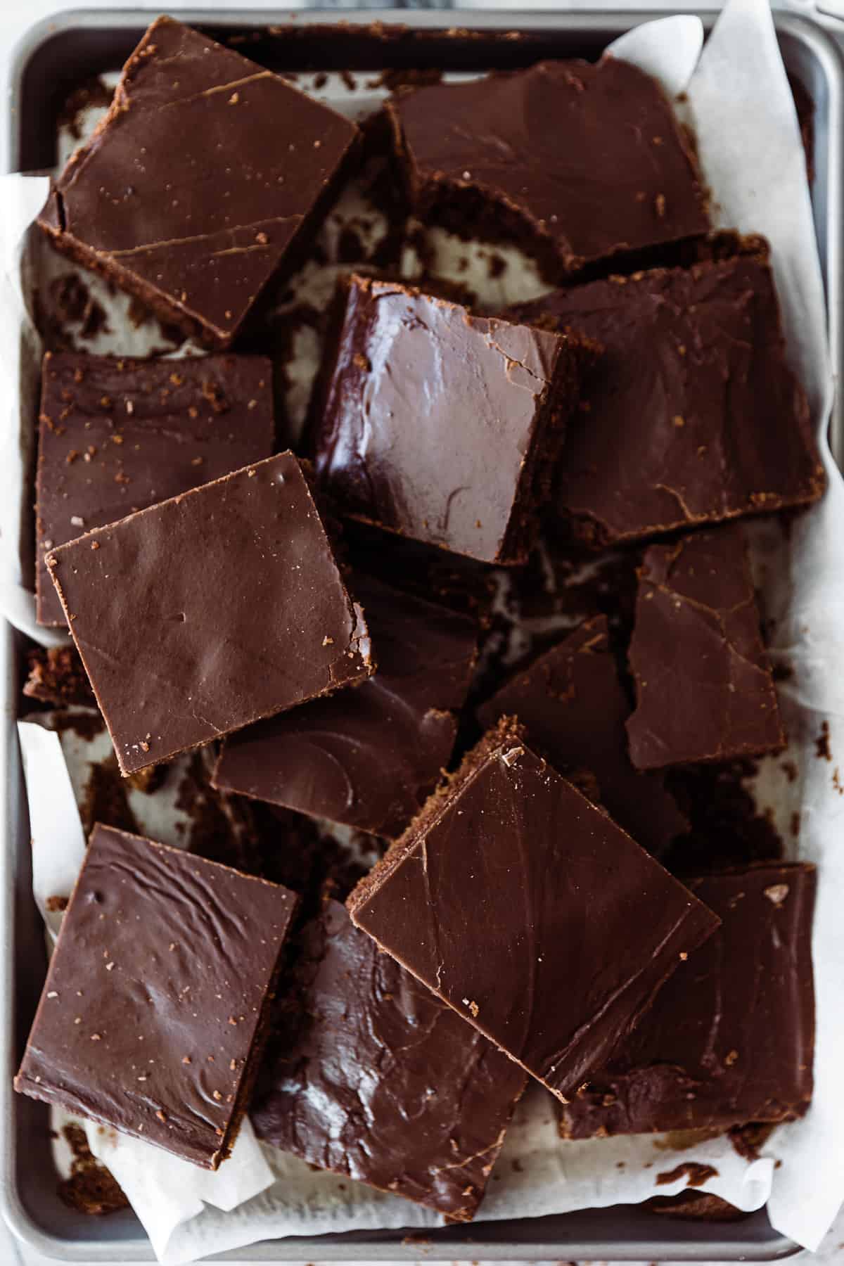 Sliced chocolate sheet cake piled onto a baking sheet with parchment paper. 