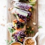 Homemade fresh rice paper spring rolls on a cutting board with thai peanut sauce.