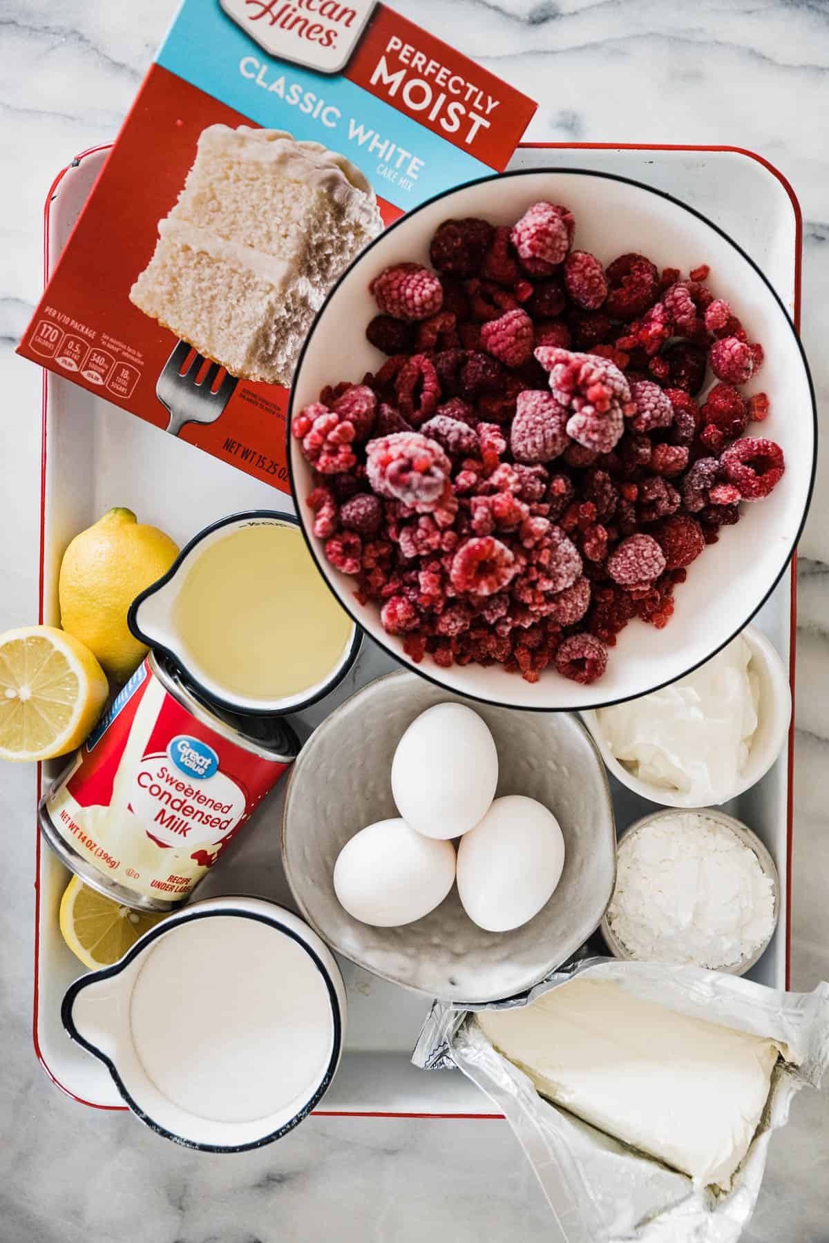 Frozen raspberries, cake mix, oil, eggs, sour cream, and lemon on a white sheet pan.