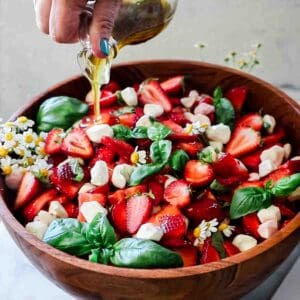 Strawberry caprese salad in a wooden bowl. Dressing is being poured on top.