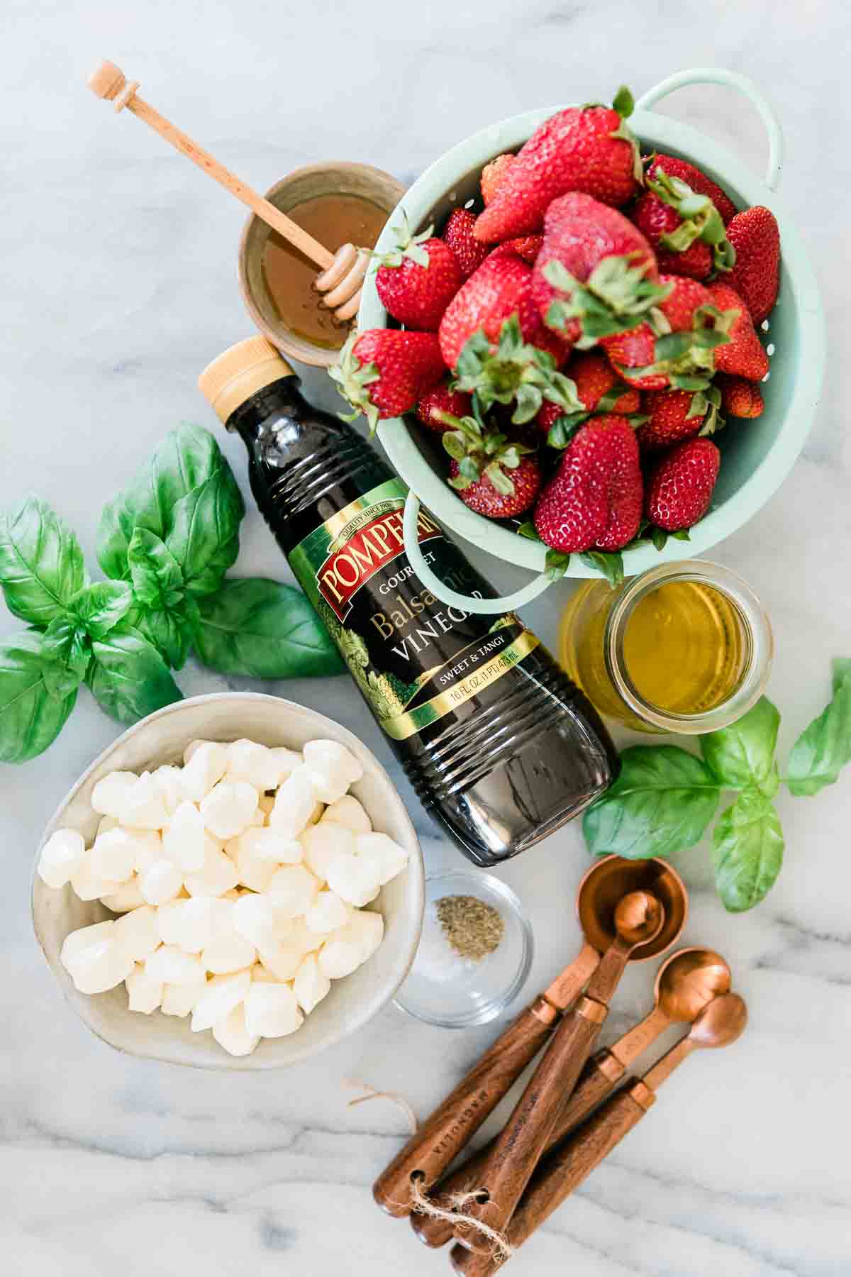 Strawberries, balsamic, mozzarella pearls, honey, oil, and basil on a marble counter.