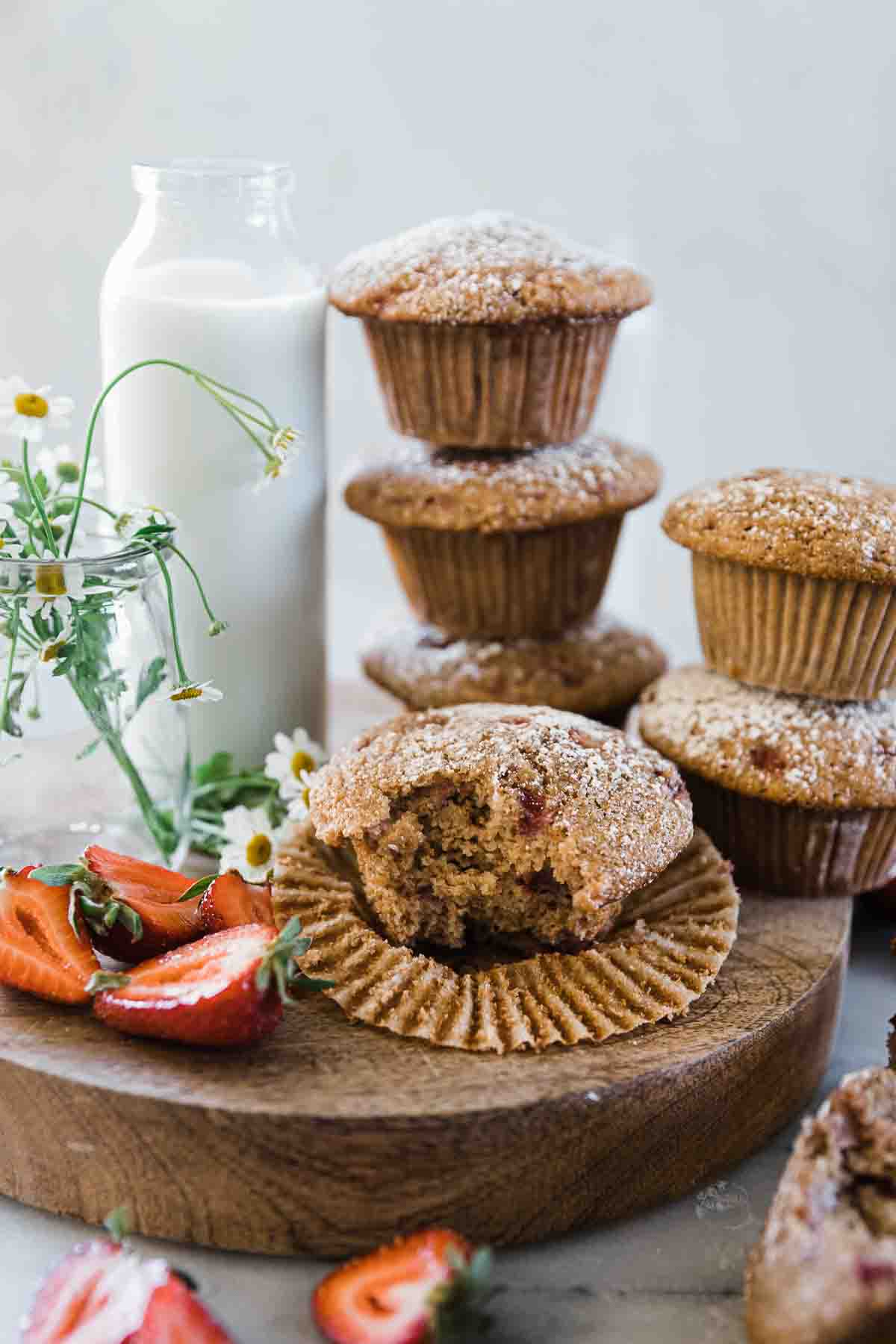 Oat bran muffins stacked on a wooden board next to a glass of milk.