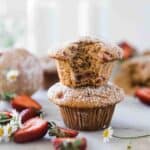 Healthy strawberry muffins stacked two high. There are sliced strawberries to the side.