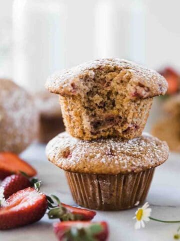 Healthy strawberry muffins stacked two high. There are sliced strawberries to the side.