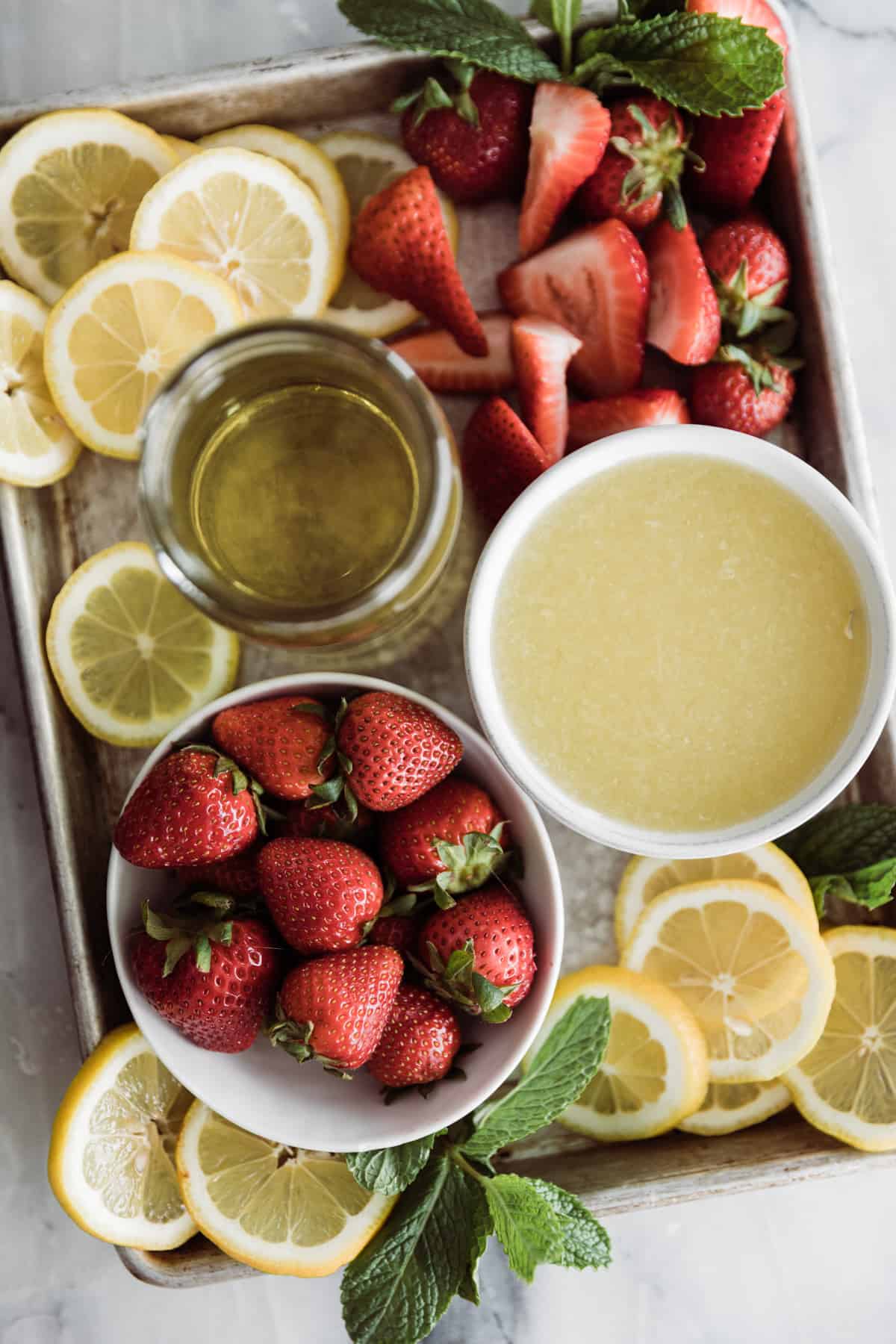 Bowl of strawberries, bowl of lemon juice, lemon slices and simple syrup on a tray. 