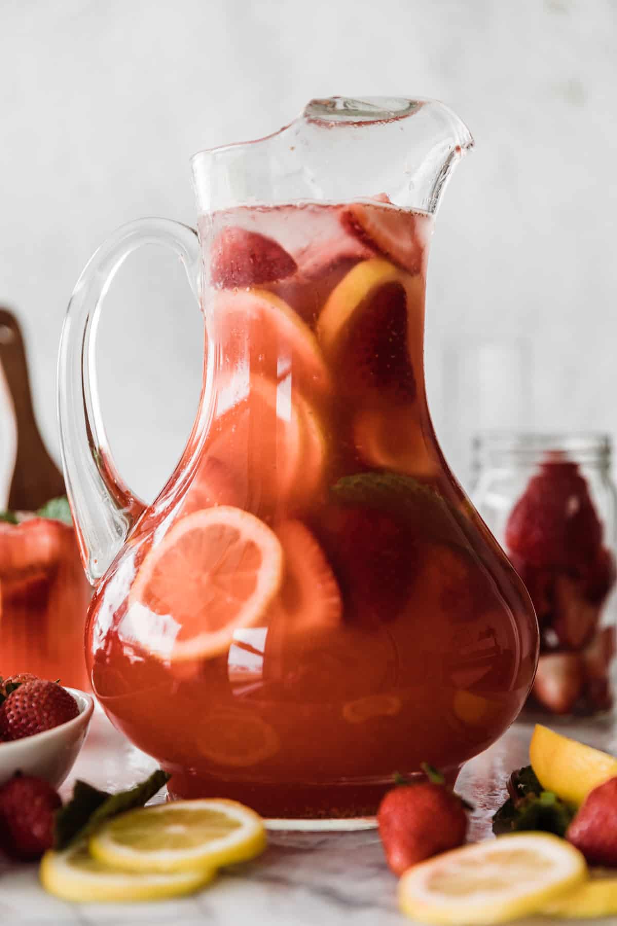 Glass pitcher filled with strawberry lemonade, fresh strawberries and lemon slices. 