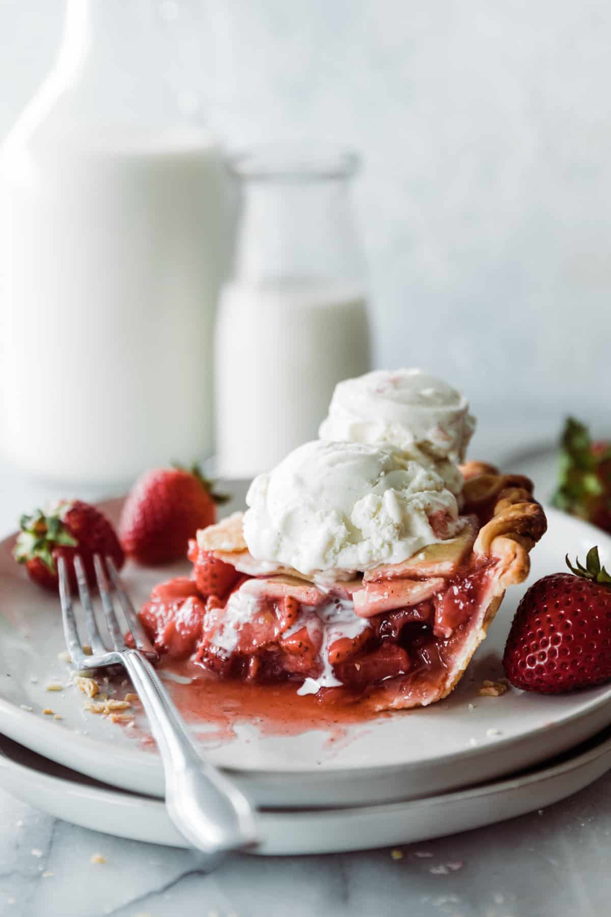 Slice of strawberry pie with dripping vanilla ice cream scoops on a dessert plate. 