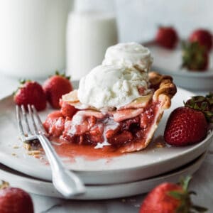 Slice of strawberry pie with ice cream on a dessert plate.