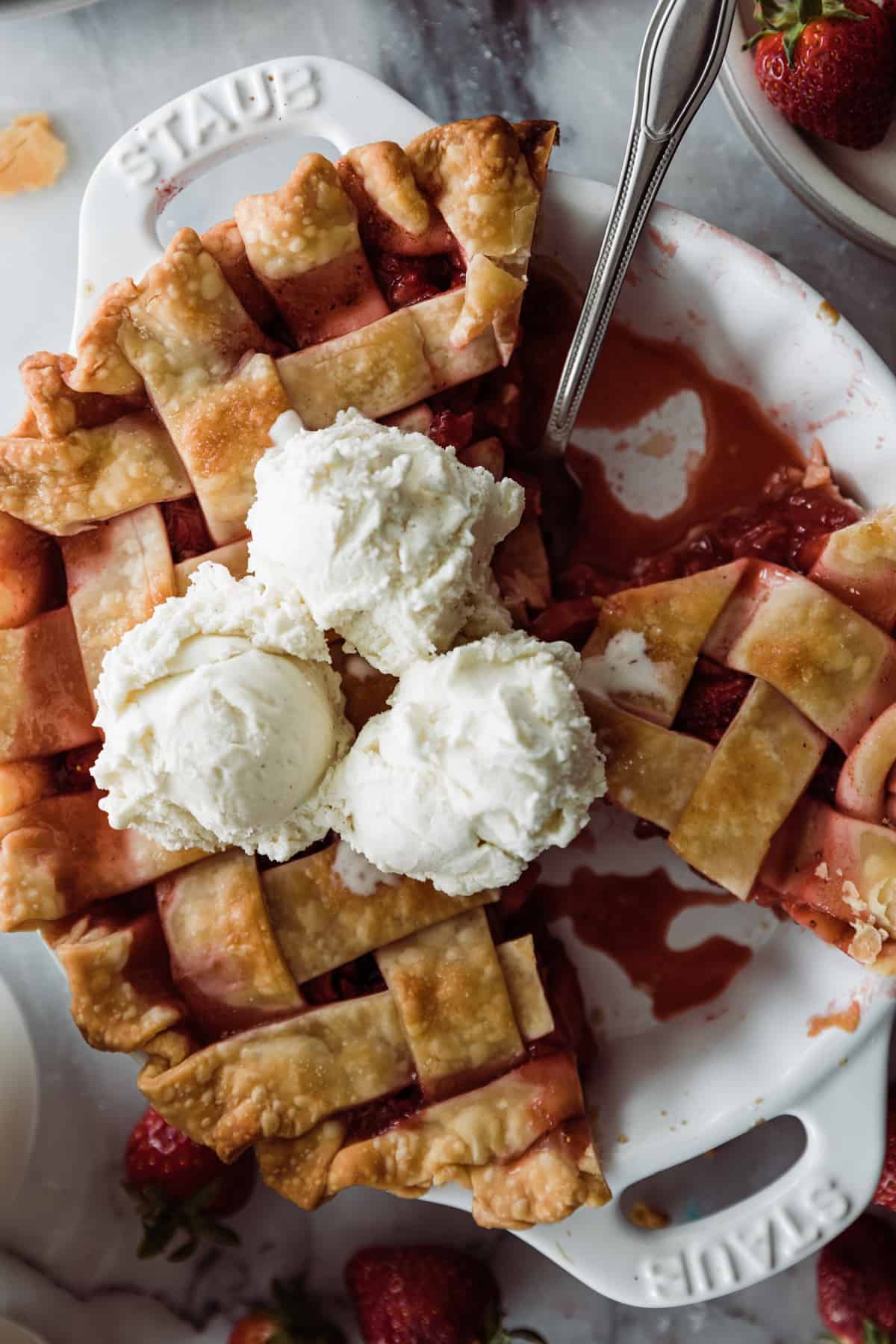 Strawberry Pie in a pie pan with two sliced removed and three scoops of vanilla ice cream. 