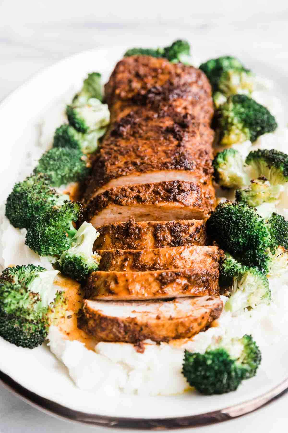 A ¾ shot of baked pork tenderloin on a bed of mashed potatoes. There is broccoli to the side.