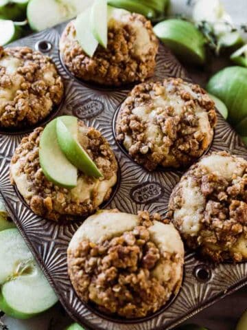 Apple muffins in a muffin tin surrounded by Granny Smith apples.