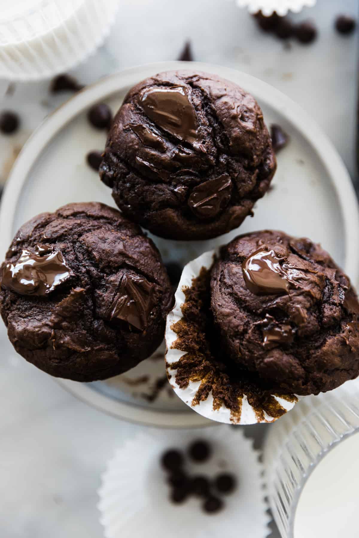 Three large chocolate chocolate chip muffins on a dessert plate. 