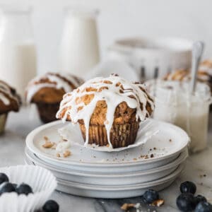 A coffee cake muffin on a white plate, drizzled with glaze. There is a bottle of milk in the background.