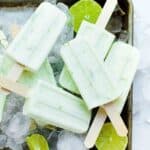 Half a sheet pan topped with lime coconut popsicles with fresh lime.