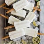 Coconut lime popsicles in different directions on ice on a tray with lime wedges.