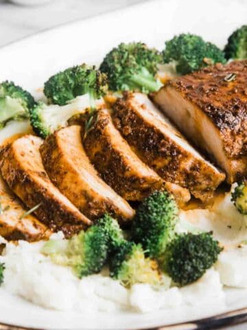 Baked pork loin on a platter atop mashed potatoes and broccoli.