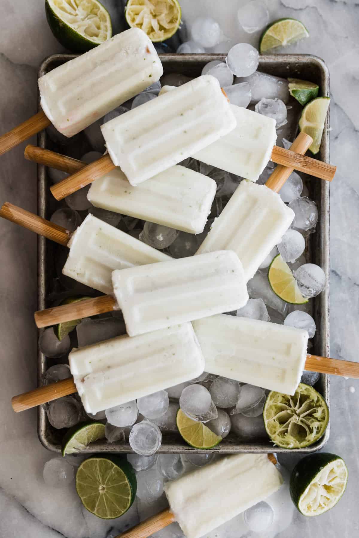 A tray of lime popsicles on a tray going in all different directions with limes and ice.
