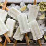 Creamy lime coconut popsicles on a tray with ice cubes and lime wedges.