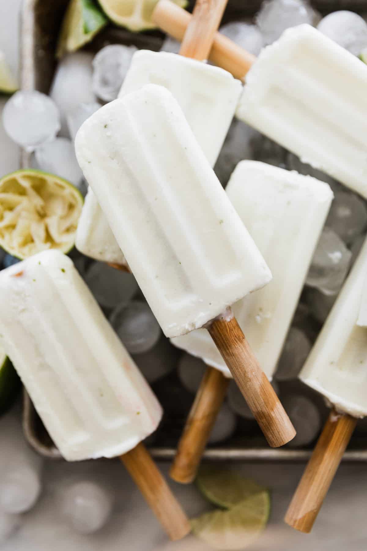 One creamy lime popsicle with round popsicle stick on other popsicles and ice. 