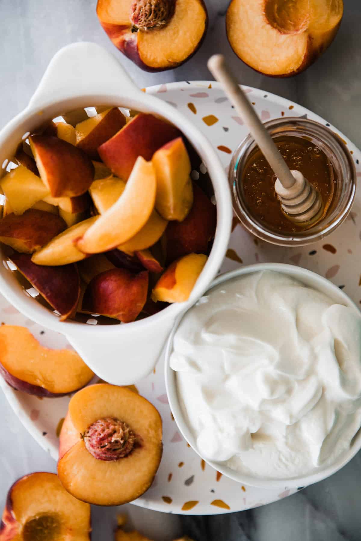 Sliced ripe peaches, greek yogurt and honey in individual bowls on a tray