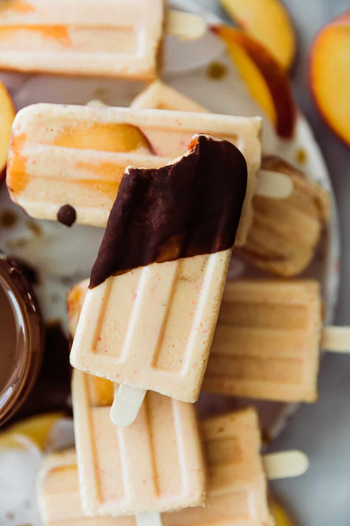 Peach popsicles on ice with one popsicle dipped in chocolate. 