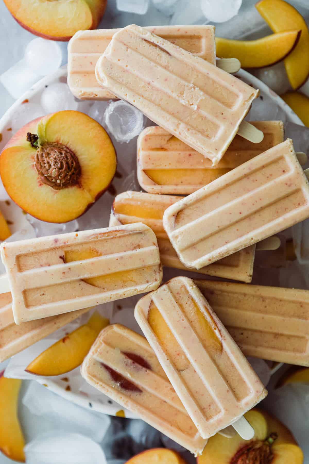 Several peach popsicles on a tray of ice with fresh peaches. 
