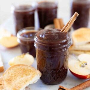 Apple butter in a mason jar. It is surrounded by sliced apples.